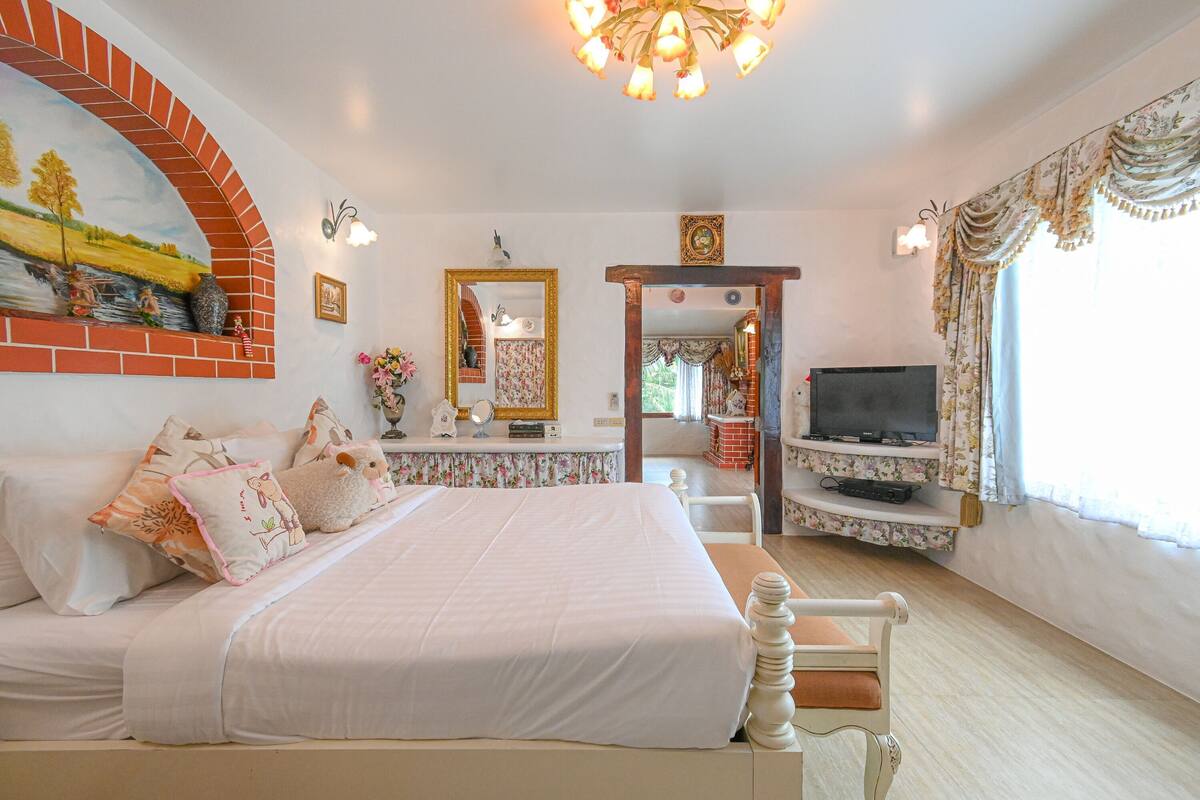 A bedroom with a large bed, a TV, a fireplace, and a mirror.