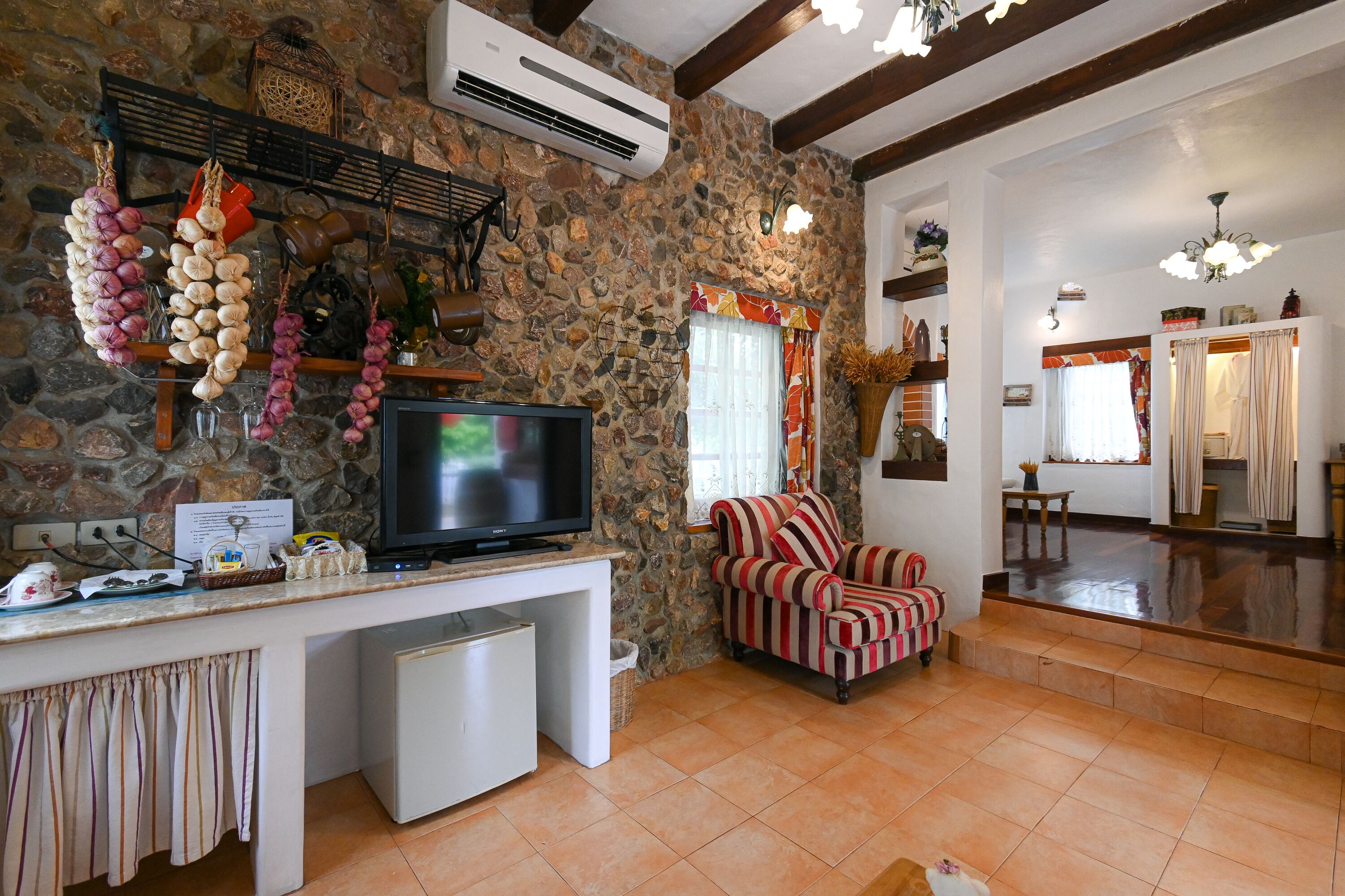 Una sala de estar con pared de piedra, un televisor, un sillón a rayas y un pequeño armario blanco.