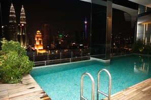Piscina en la azotea con vistas a la ciudad, incluyendo las Torres Petronas y una torre iluminada.