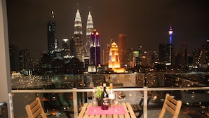 A balcony with a table set for two, overlooking a city skyline at night. - Apartment at Setia Sky Residences (Kuala Lumpur)