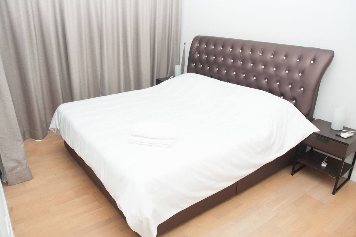 A neatly made bed with a tufted headboard, a bedside table with a lamp, and a wooden floor.
