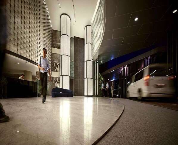 Un vestíbulo de hotel moderno con suelo curvo, grandes columnas cilíndricas y un revestimiento de pared con diseño.
