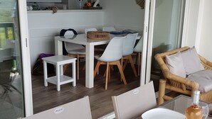 Uma área de refeições com uma mesa posta para quatro pessoas, uma garrafa de vinho e copos de vinho vazios. Há uma cesta de vime na mesa e um relógio na parede.