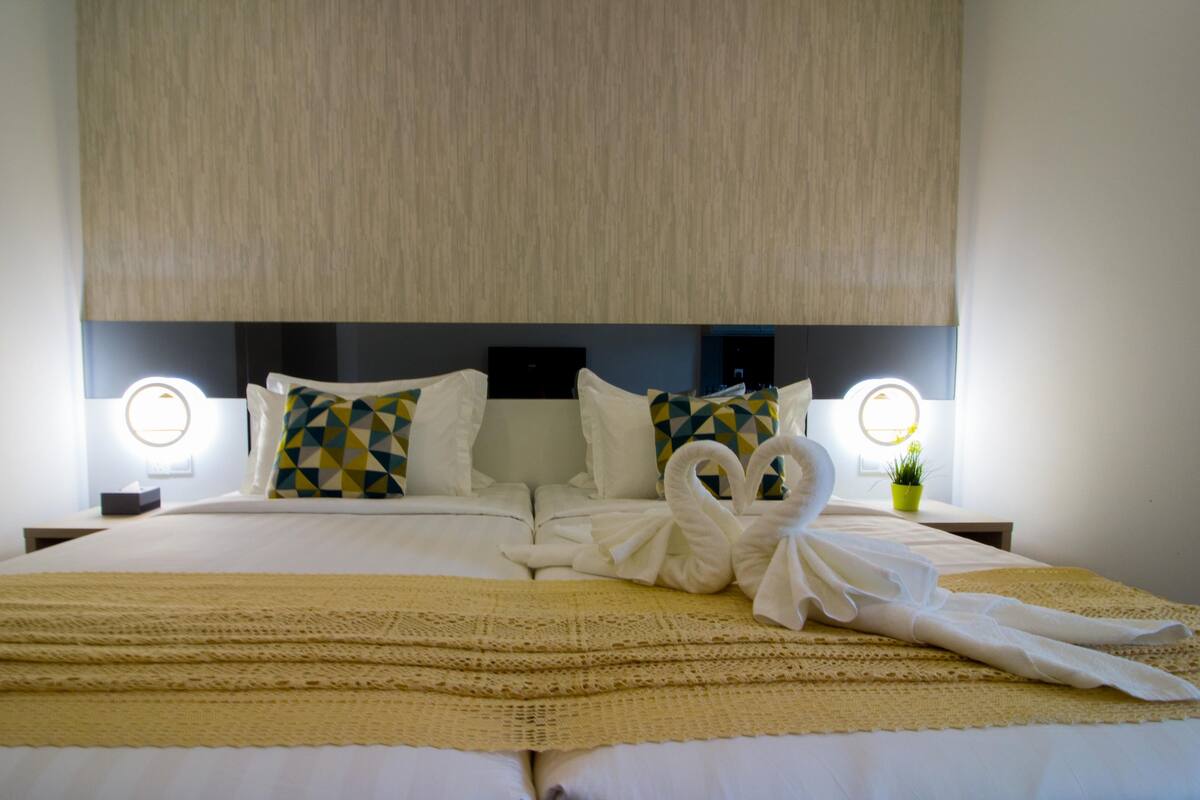 A neatly made bed with a decorative towel arrangement, a bedside lamp, and a potted plant.