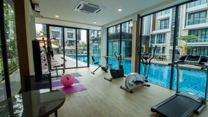 A gym with exercise equipment, a pink exercise ball, and a pool in the background. - Tropical Villa Service Suite (Seri Kembangan)