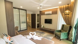 A modern hotel room with a large bed, a TV, a green armchair, and a ceiling fan. - Tropical Villa Service Suite (Seri Kembangan)
