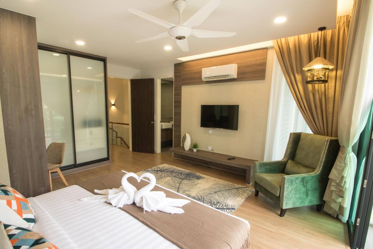A modern hotel room with a large bed, a TV, a green armchair, and a ceiling fan.