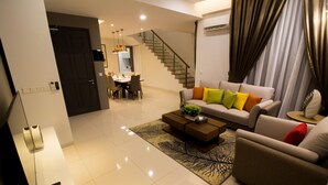 A modern living room with a sofa, coffee table, and a dining area in the background. - Tropical Villa Service Suite (Seri Kembangan)