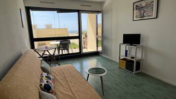 Een woonkamer met een bank, een klein rond tafeltje en een tv-meubel.