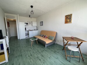Un espacio habitable compacto con kitchenette, un sofá, una mesita redonda y una silla.