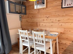 A dining area with a wooden table and white chairs, a mirror, and a framed picture on the wall.