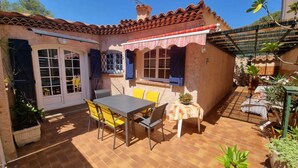 Un patio con una mesa y sillas, una pequeña mesa con un arreglo floral, y una pérgola con un toldo a rayas.