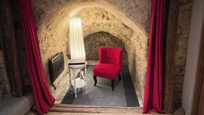 Habitació acollidora amb un arc de pedra, una cadira vermella, una taula amb una làmpada i un radiador.