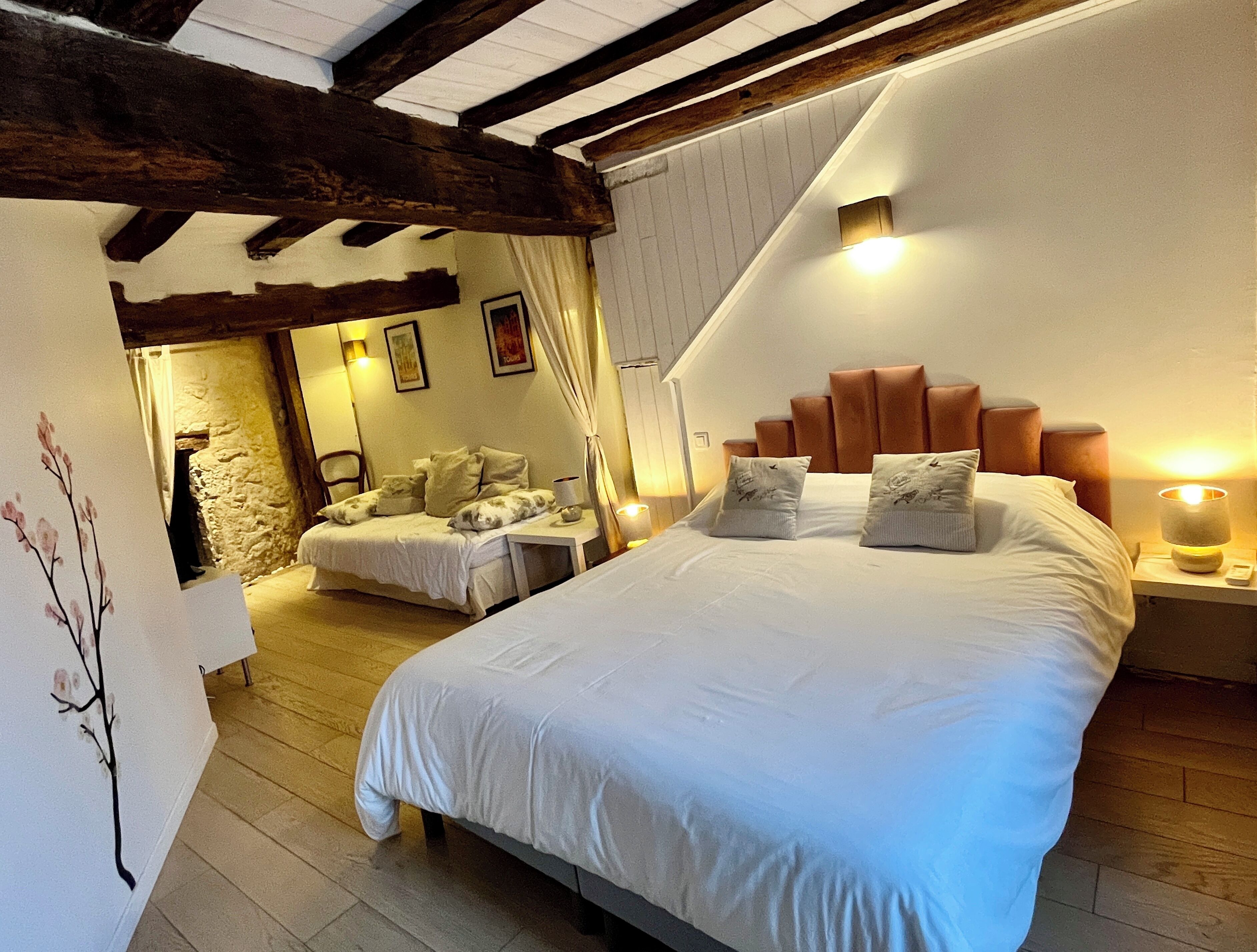 Une chambre avec un grand lit, un plus petit lit, des poutres en bois, un mur en pierre et un tableau.