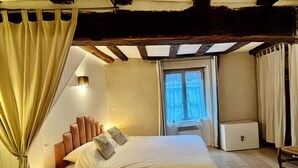 Un dormitori amb un llit, una taula de nit, una finestra amb cortines i un petit armari.