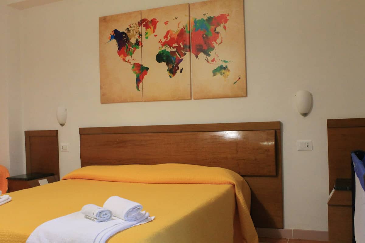 Quarto de hotel com cabeceira de madeira, uma cama grande com colcha laranja e uma obra de arte de mapa-múndi na parede.