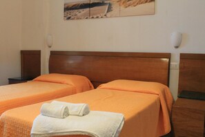 A hotel room with two beds, each with an orange bedspread and a white towel folded on top.