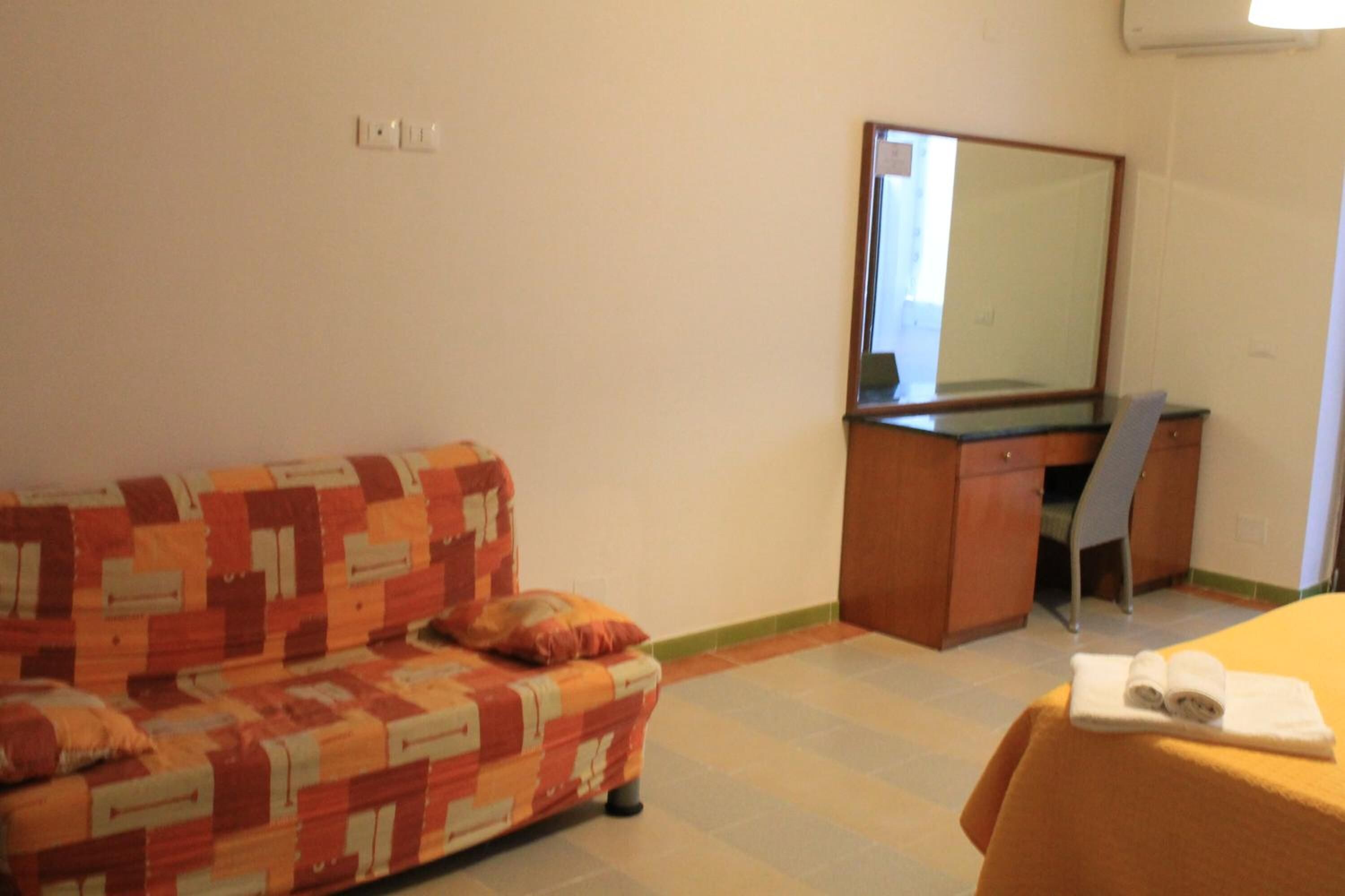 A hotel room with a sofa, a desk, a chair, and a bed with a towel on it.