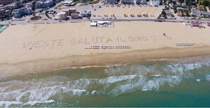 An aerial view of a beach with the words "WESTE SALUTA IL GIRO DI M" etched into the sand.