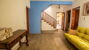 Un couloir avec un escalier en bois, un canapé jaune et une table en bois ornée d’objets décoratifs.