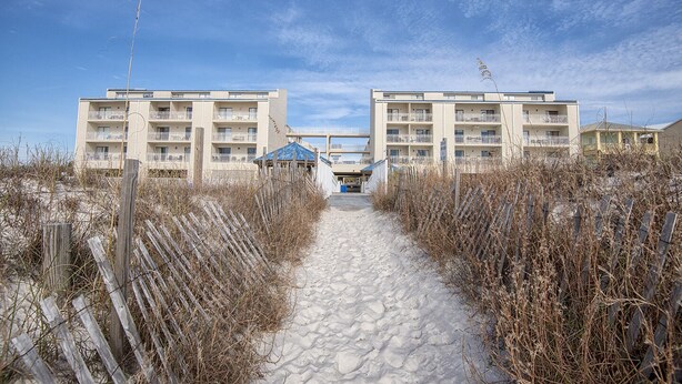 A pathway leading to a beachfront building with multiple balconies and a blue-roofed structure in the center.