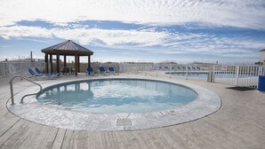 A swimming pool with lounge chairs and a gazebo, surrounded by a wooden deck and a fence.