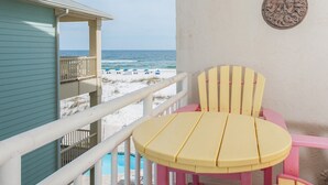 A balcony with a view of the beach and ocean, a round yellow table, and a pink chair.
