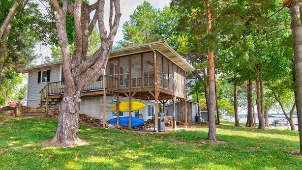 Une maison à deux étages avec un balcon, entourée d’arbres et bordée d’une pelouse.