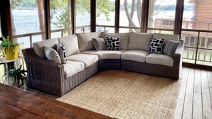 Un canapé d’angle avec des coussins à motifs, un tapis tissé et une vue sur un lac, visible à travers de grandes fenêtres.