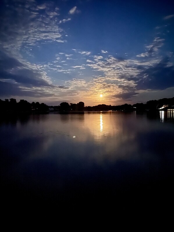 A calm lake at sunset with a clear sky and distant trees.