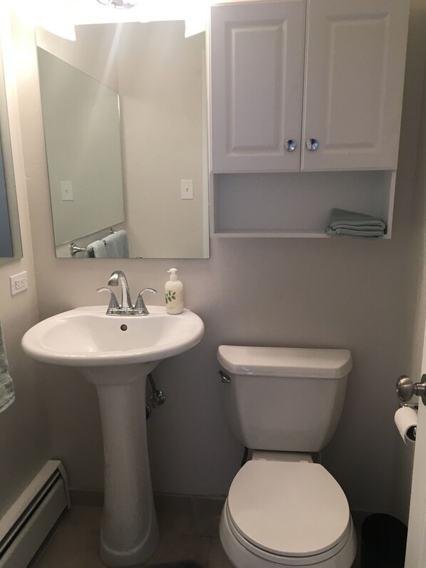 Un baño con lavamanos pedestal, inodoro y un armario sobre el lavamanos.