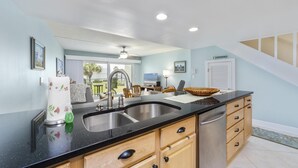 A kitchen with a black countertop, wooden cabinets, and a sink. There is a ceiling fan and recessed lighting.