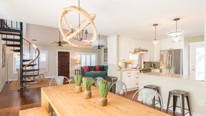Una cocina moderna con armarios blancos, electrodomésticos de acero inoxidable y una mesa de comedor de madera con plantas en macetas.