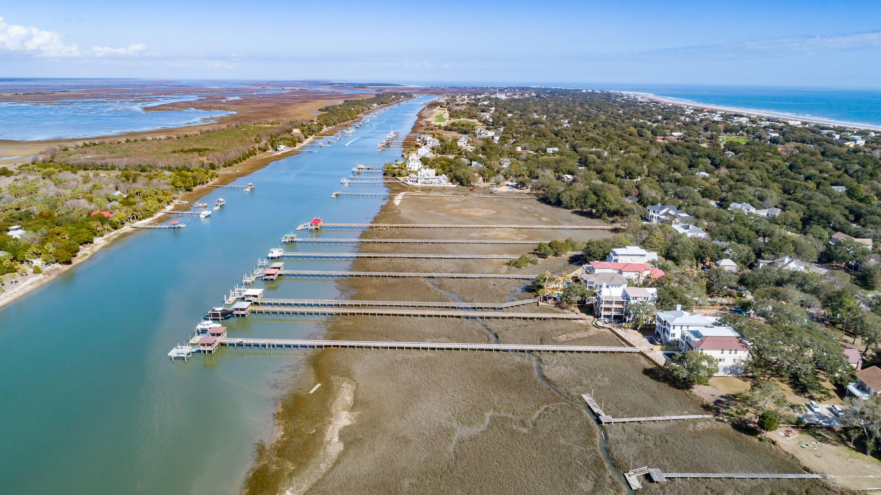 An aerial view of a coastal area with a marina, houses, and a beach.