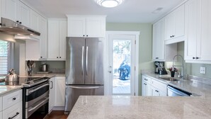 Una cocina moderna con armarios blancos, electrodomésticos de acero inoxidable, encimera de granito y vistas al exterior.