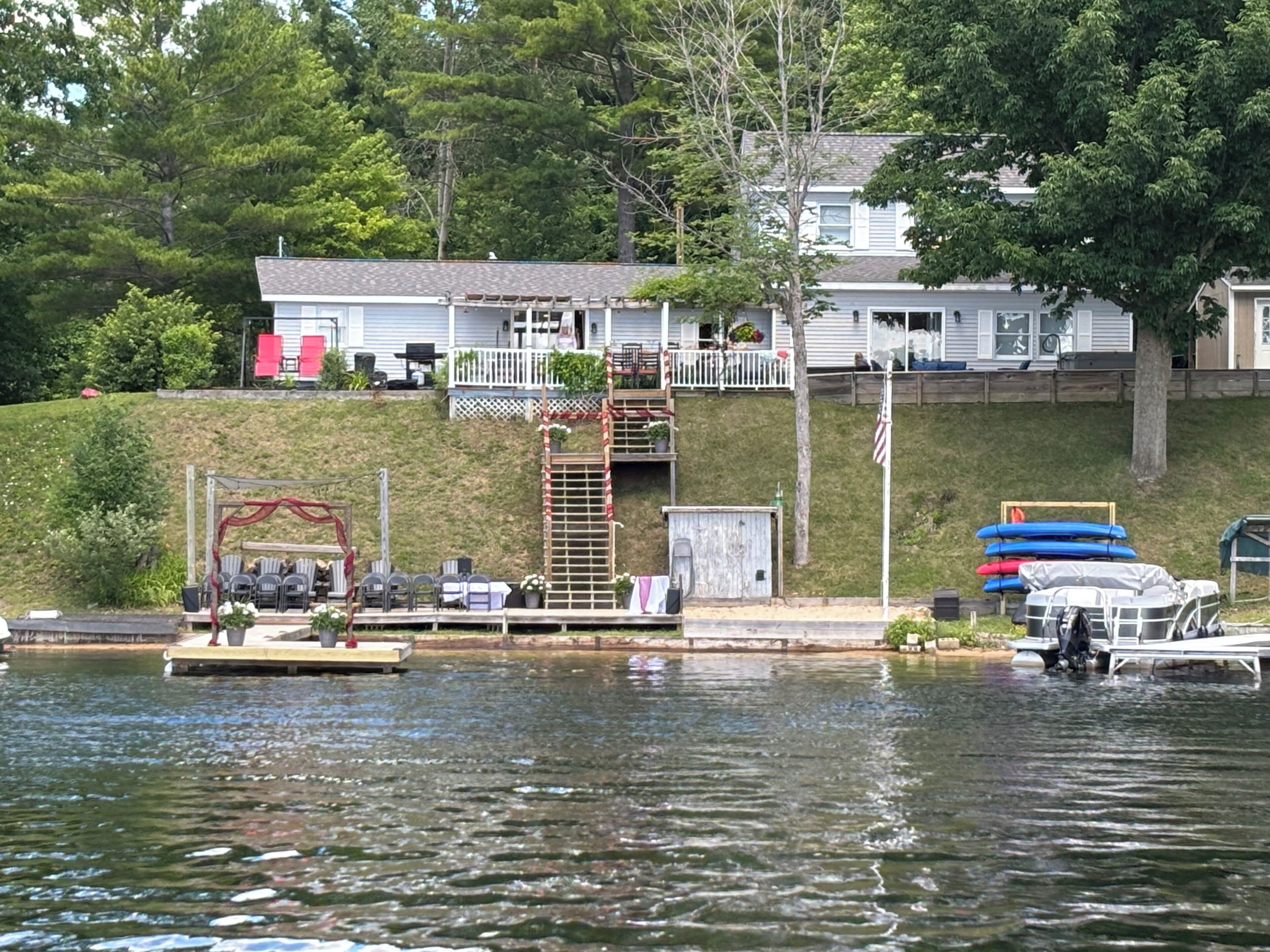 A lakeside property with a dock, a small boat, and a house with a porch.