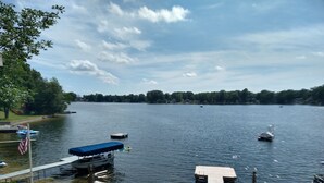 Ein Seeufer mit Booten, einer überdachten Sitzgelegenheit und Blick auf den See.
