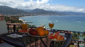 A table with fruit and drinks, overlooking a coastal city and mountains. - Oceanfront 2 Bedroom, Spectacular Ocean Views, 59.00/nt May-Oct, monthly rental (Puerto Vallarta)