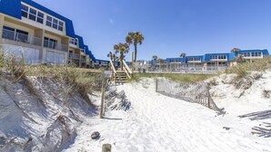 A beachfront hotel with multiple blue and beige buildings, a sandy beach, and palm trees. - Sandpiper 109 - Ground floor with all the upgrades! (St. Augustine)