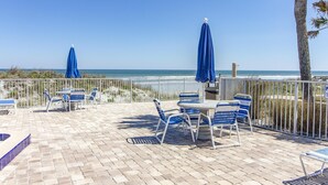 An outdoor patio with blue chairs and umbrellas, a pool, and a view of the ocean. - Sandpiper 109 - Ground floor with all the upgrades! (St. Augustine)