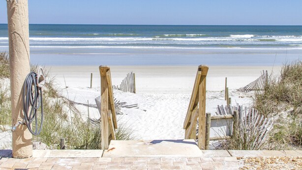 A beach entrance with a wooden pathway leading to the shore, a concrete post with a hose, and a sandy beach with a wooden fence. - Sandpiper 109 - Ground floor with all the upgrades! (St. Augustine)