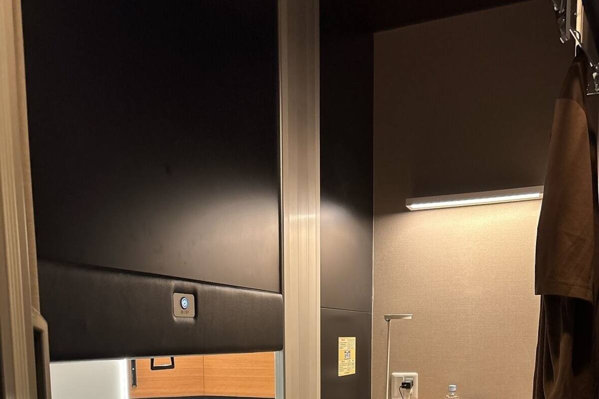 Une chambre d’hôtel de taille réduite, comprenant un lit, un petit bureau, un miroir et une poubelle.