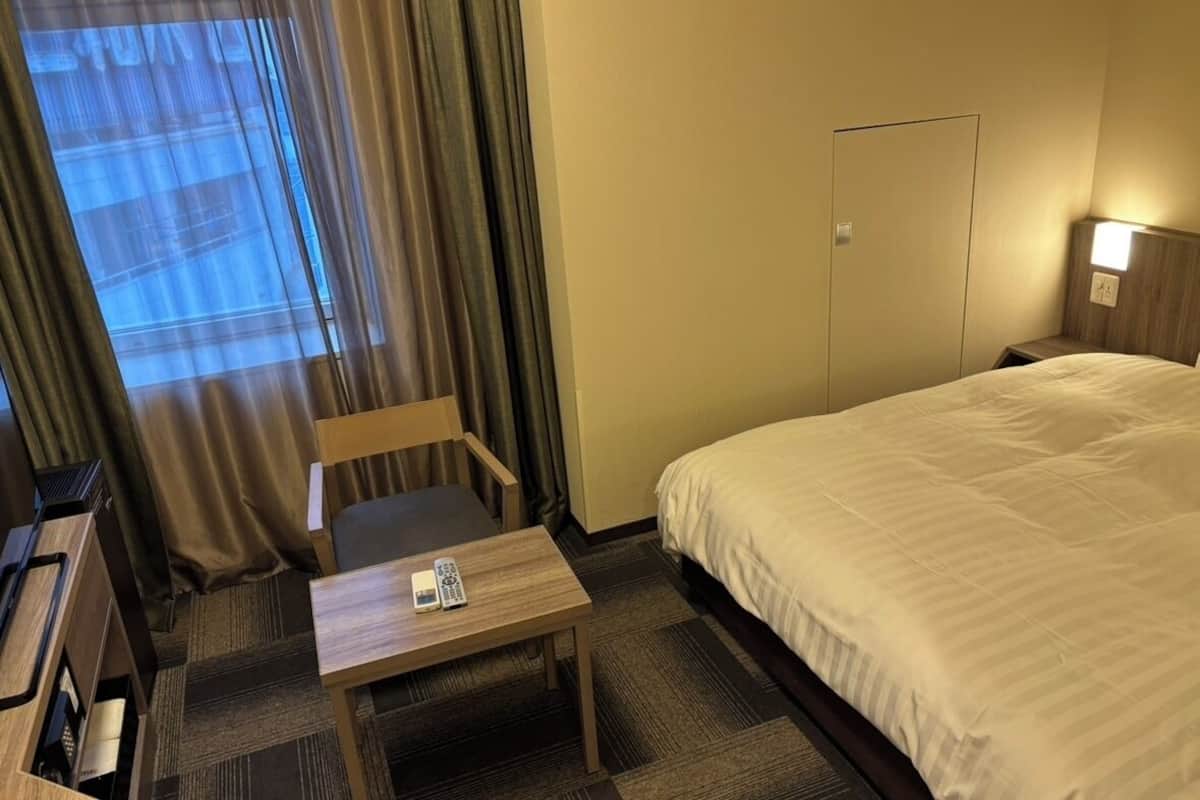 Une chambre d’hôtel avec un lit, un bureau avec un téléphone, une chaise, une fenêtre avec des rideaux et une porte.