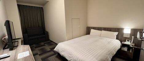 A hotel room with a bed, a desk, a television, and a nightstand.