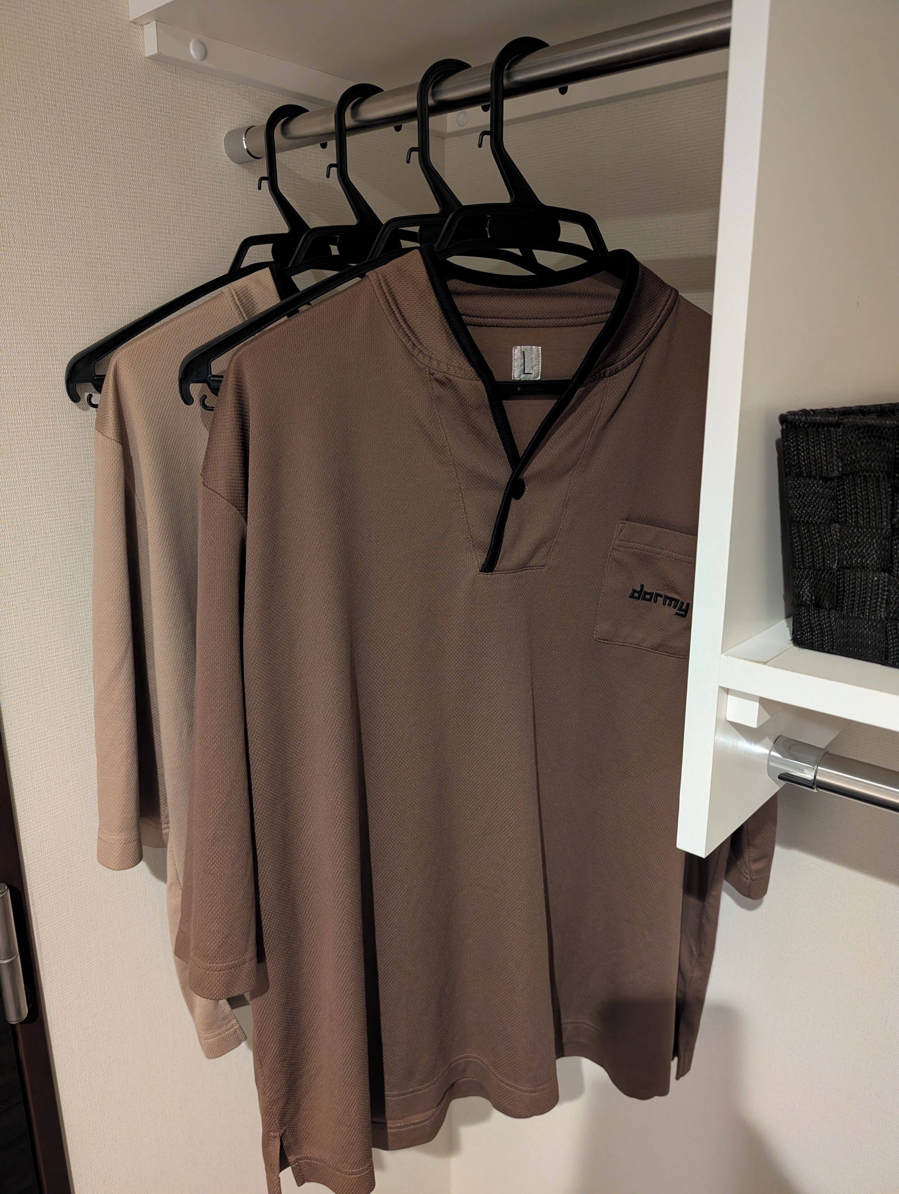 A closet with hanging clothes and a shelf with a black bag.