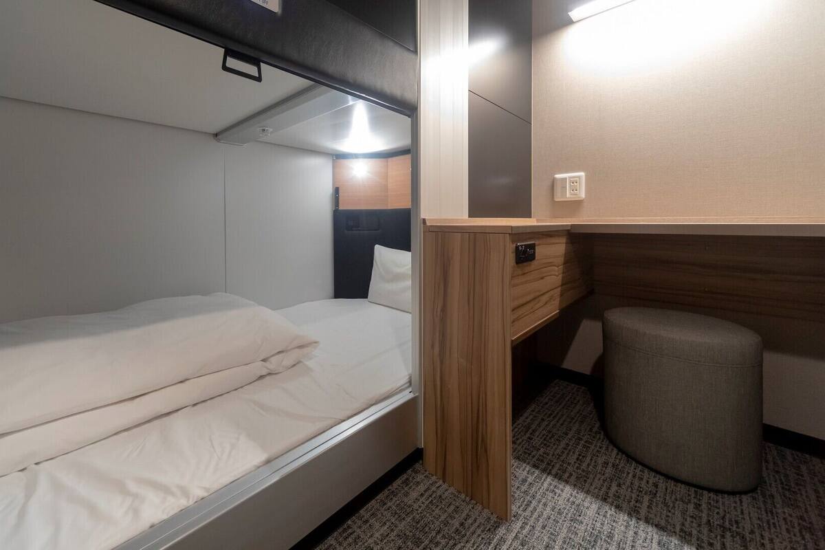 A compact, well-lit bedroom with a single bed, a small desk, and a storage cabinet.