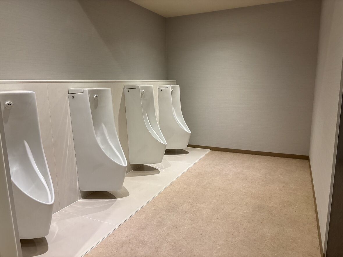 A row of white urinals in a restroom with a beige floor and plain walls.