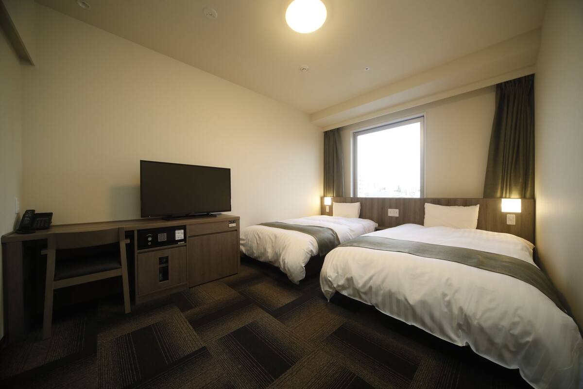 Une chambre d’hôtel avec deux lits, un téléviseur posé sur un meuble en bois et un bureau avec un téléphone.