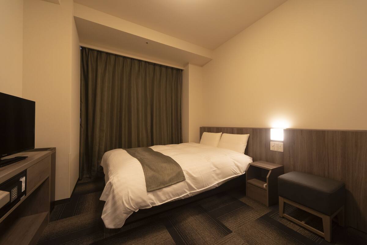 Une chambre d’hôtel avec un lit, une table de chevet, une télévision et un petit banc.