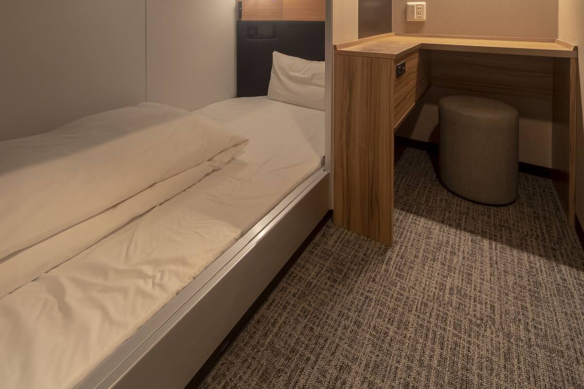 Une chambre d’hôtel de taille réduite, comprenant un lit simple, un petit bureau et une chaise.